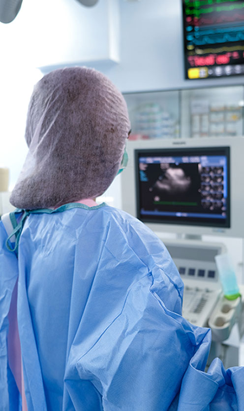 The backside image of a medical professional operating and monitoring an echocardiography machine.